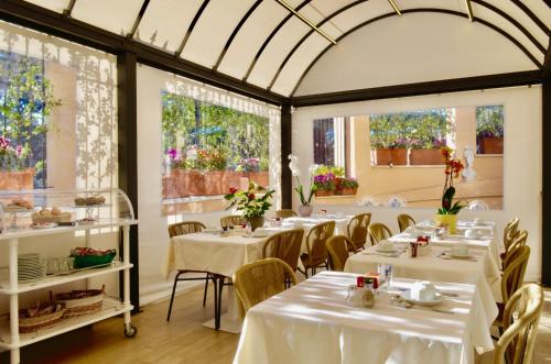 un restaurante con mesas y sillas blancas y ventanas en Sourire Hotel, en Roma