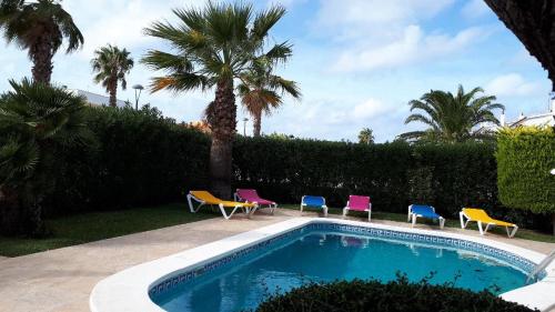 a swimming pool with colorful chairs and palm trees at Villa Desi in Cala en Blanes