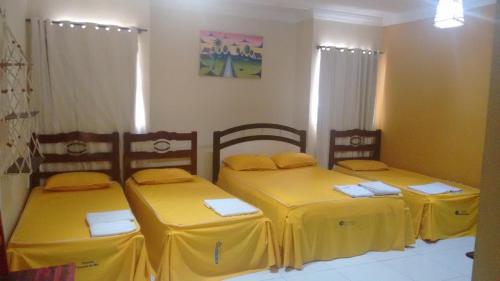 a room with three beds with yellow sheets at Pousada Aquino in Sobral