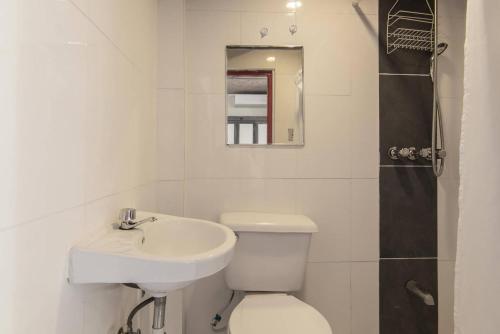 een badkamer met een toilet, een wastafel en een spiegel bij La Puerta Roja Guest House in Santo Domingo