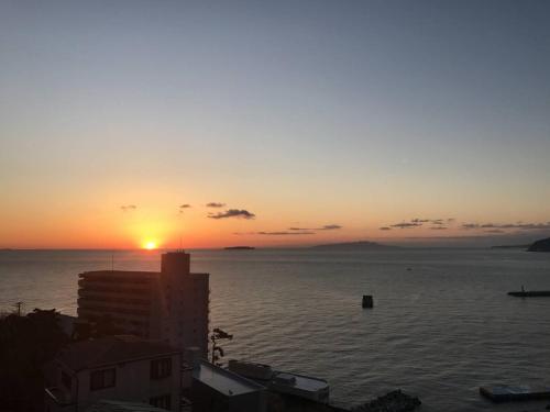 una puesta de sol sobre el agua con un edificio en primer plano en Atami Onsen Guest House Megumi, en Atami