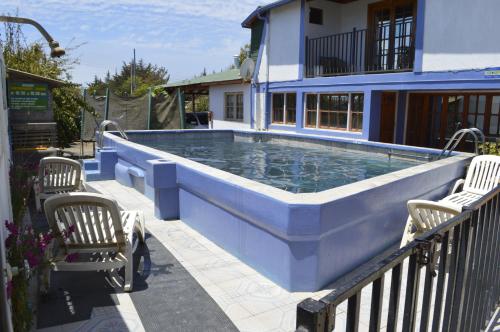 una gran piscina azul con 2 sillas y una casa en Cabañas Hecmar, en Pichilemu