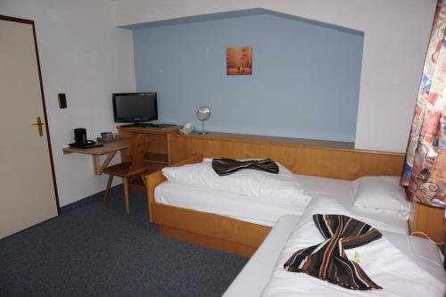 a room with two beds and a desk with a television at Hotel Untermetzger in Zell am Ziller