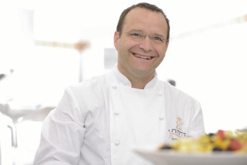 a man in a chefs outfit holding a plate of food at Hotel Erbprinz - Gourmet & Spa in Ettlingen