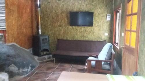 sala de estar con sofá y TV en la pared en Cabaña Modesto, en Olmué