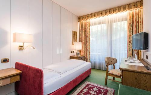 a hotel room with a bed and a desk and a television at Hotel Grüner Baum in Bressanone