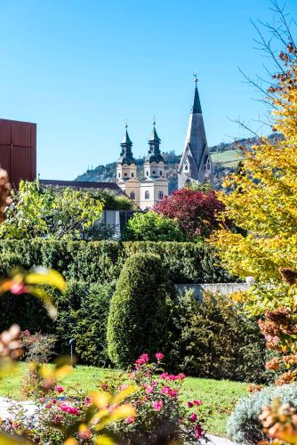 a building behind a hedge with a church in the background at Hotel Grüner Baum in Bressanone