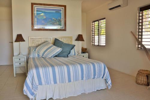 a bedroom with a bed with a striped comforter and two windows at Banfields Retreat in Mission Beach