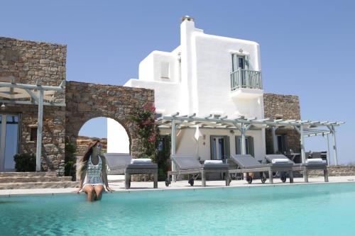 a woman sitting on the edge of a pool in front of a house at Niriides Homes & Villas in Elia Beach