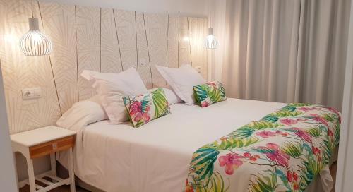 a bedroom with a bed with white sheets and tropical pillows at Apartamentos Gelimar in Puerto Rico de Gran Canaria