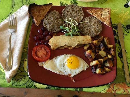 a plate of breakfast food with eggs sausage and bread at Gîte Au Coin De La Berge in Perce