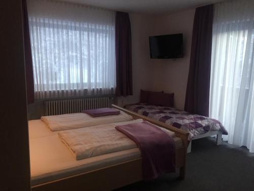two beds in a room with a tv and windows at Gästehaus Wagner in Grainau