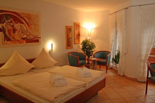 a bedroom with a bed with white sheets and chairs at Hostellerie Bacher in Neunkirchen