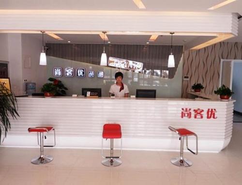 una mujer de pie detrás de un mostrador con taburetes rojos en Thank Inn Chain Hotel Shandong Shouguang New Bus Station, en Shouguang
