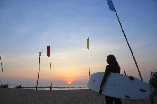 a woman standing on the beach holding a surfboard at Manel Villa in Bentota