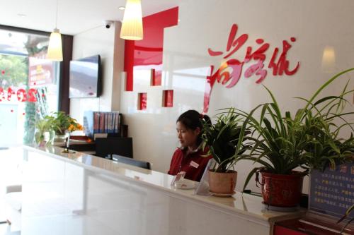 Thank Inn Chain Hotel Jiangsu Nantong Jiuwei Bay في نانتونغ: امرأة تجلس في كونتر في مطعم