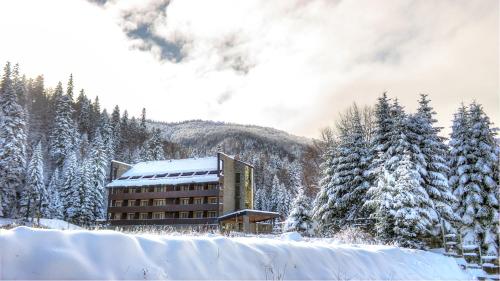 a building covered in snow in front of a mountain at Lux Garden Hotel in Azuga