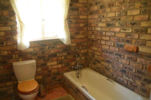 a brick walled bathroom with a toilet and a bath tub at Thaba Tsweni Lodge & Safaris in Graskop