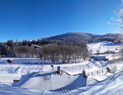 a snow covered field with houses and a mountain at Chata Ramzovské sedlo in Ramzová