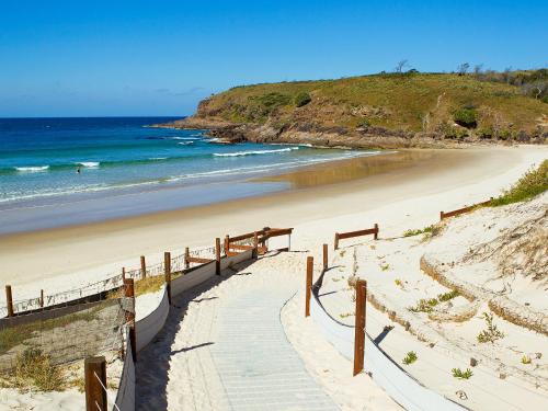 a stairway leading to a sandy beach with the ocean at Grassy Head Holiday Park in Stuarts Point
