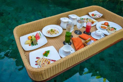 a table with food and drinks on a table in the water at Purana Boutique Resort in Ubud