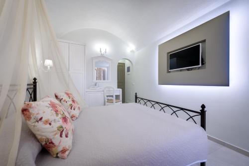 a white bedroom with a bed and a tv at Zephyros Hotel in Kamari