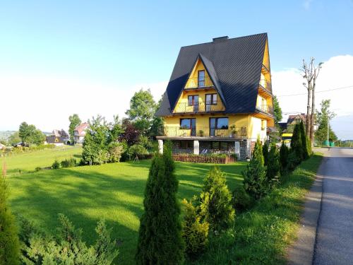 a yellow house with a black roof on a green lawn at Apartamenty u Klisia in Ząb