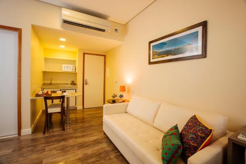 a living room with a white couch and a kitchen at Intercity Suape Costa Dourada in Cabo de Santo Agostinho
