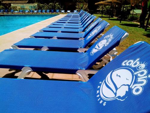 a row of blue lounge chairs next to a swimming pool at Complejo Turístico & Camping Cabopino in Marbella