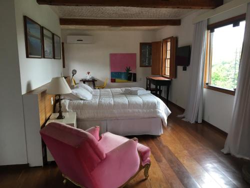 - une chambre avec deux lits et une chaise rose dans l'établissement Pousada Casa das Fontes, à Tiradentes