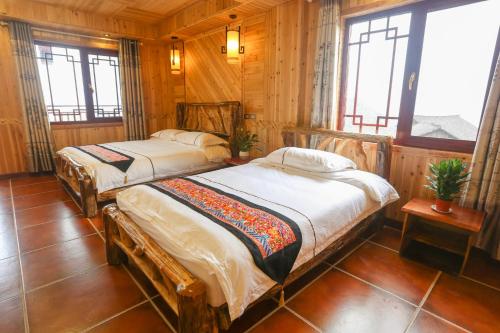 two beds in a room with wooden walls and windows at Longji Holiday Hotel in Longsheng