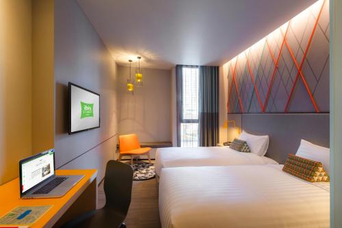 a hotel room with two beds and a desk with a laptop at ibis Styles Bangkok Sukhumvit Phra Khanong in Bangkok