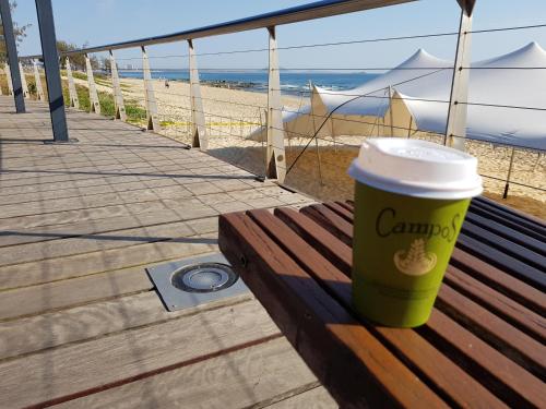 a cup of coffee sitting on a bench next to the beach at Excellsior Apartments in Mooloolaba