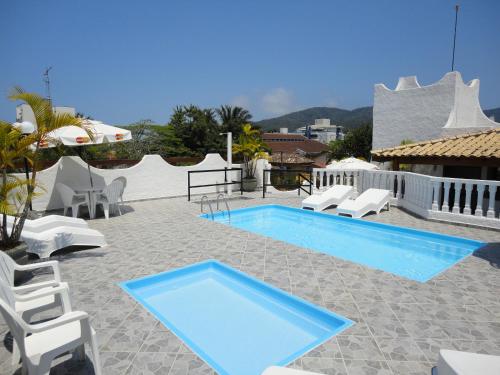 a swimming pool with white chairs and a blue poolvisor at Pousada Torre Del Mar in Ubatuba