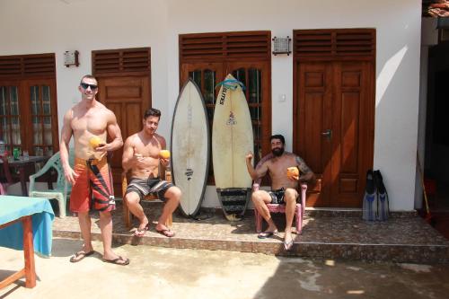 three men sitting in front of a house with surfboards at Sanda Hiru Guest in Mirissa