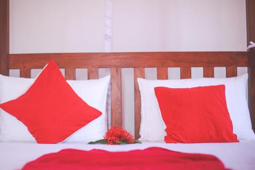 a bed with red pillows and a red flower on it at Lazies Midigama in Midigama