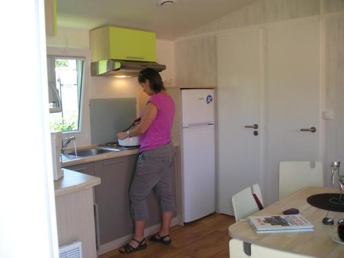 a woman standing in a kitchen preparing food at Camping Base de Loisirs du Lac de la Moselotte in Saulxures-sur-Moselotte