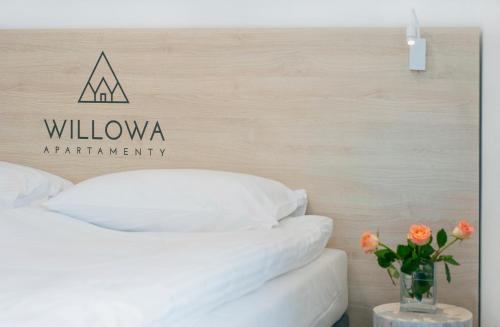 a bed with white sheets and a vase with orange flowers at Apartamenty Willowa in Szczyrk