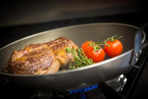 a steak in a pan with tomatoes on the stove at Hotel Rhodos Morzine in Morzine