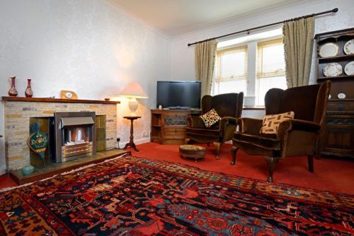 a living room with a fireplace and chairs and a tv at Granny’s Cottage in Newcastleton