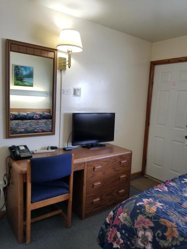 a hotel room with a desk with a television and a bed at Home Motel Abbotsford in Abbotsford
