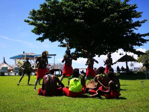 a group of people sitting on the grass under a tree at Rapopo Plantation Resort in Kokopo