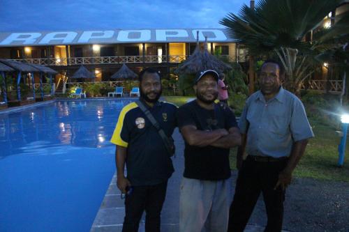 a group of three men standing next to a pool at Rapopo Plantation Resort in Kokopo