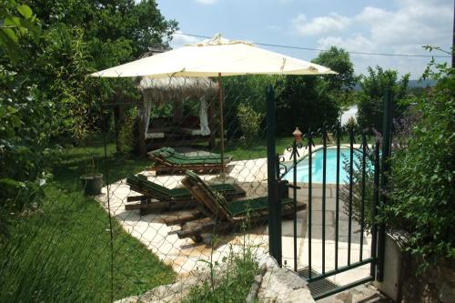 a fence with chairs and an umbrella next to a pool at Gite La Paillote in Montauroux