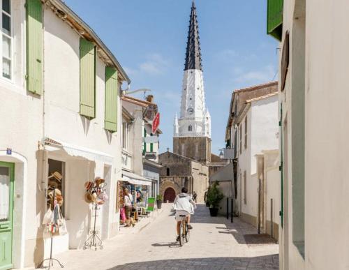 a person riding a bike down a street with a church at Les Nuits Bleues in Ars-en-Ré