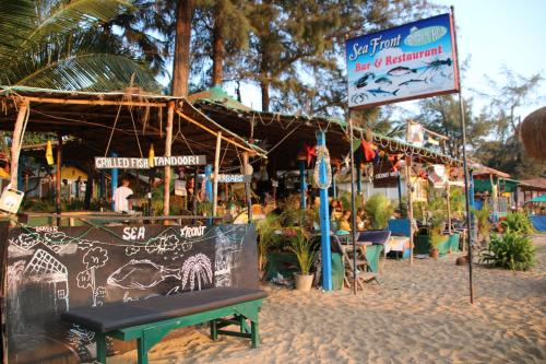 a restaurant on a beach with a bench and a sign at Sea Front Beach Huts in Patnem