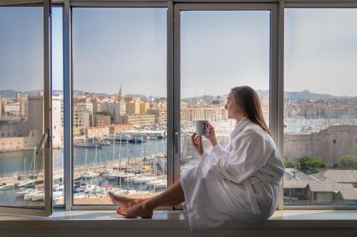 a woman sitting in a window taking a picture of a city at Sofitel Marseille Vieux-Port in Marseille