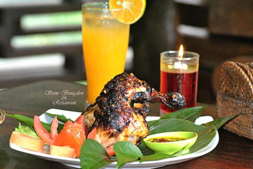 a plate of food with a chicken on a table with fruit at Sam's Bungalows in Bukit Lawang
