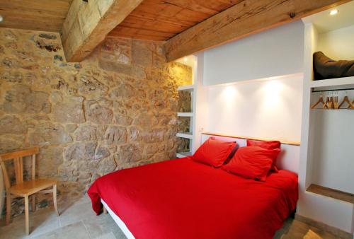 1 dormitorio con 1 cama roja en una pared de piedra en Mas des Clauzals, en Le Cros