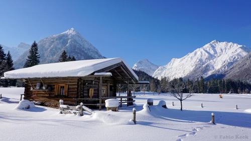 a log cabin in the snow with snow covered mountains at Apartments & Zimmer Urschnerhof in Pertisau